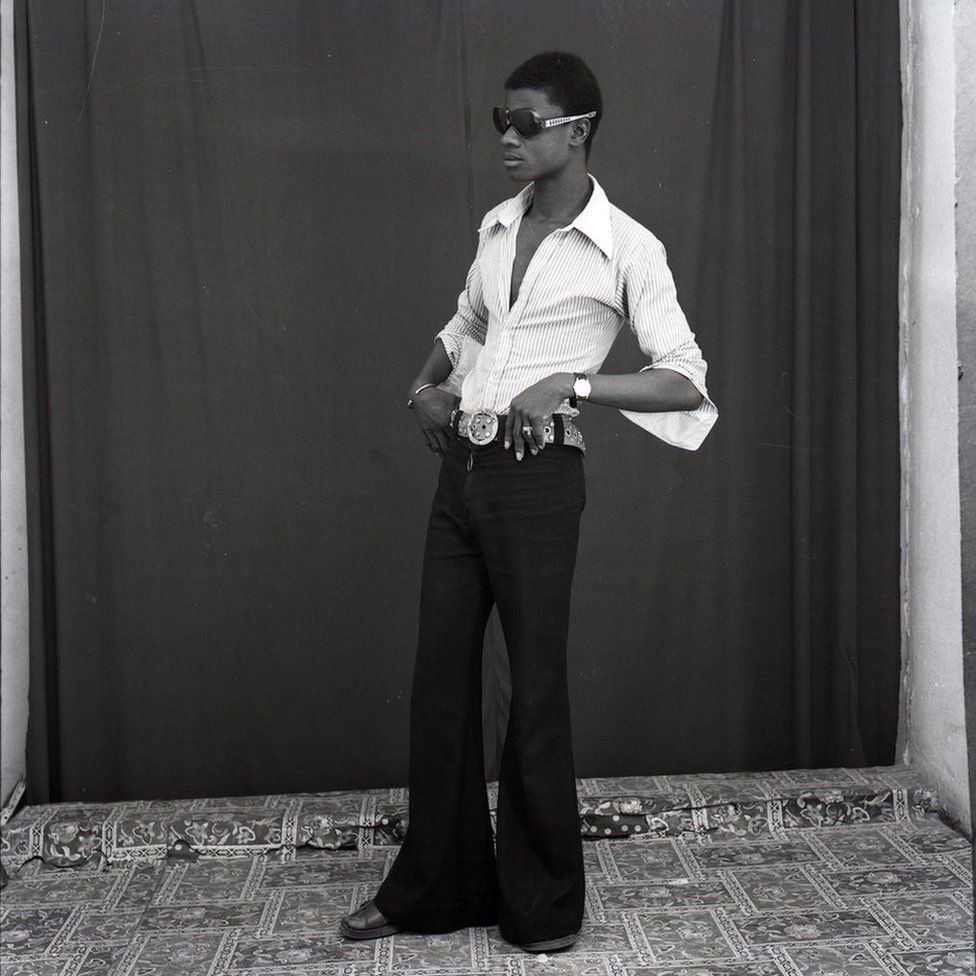 Man wearing flares and sunglasses stands with his hands on his hips