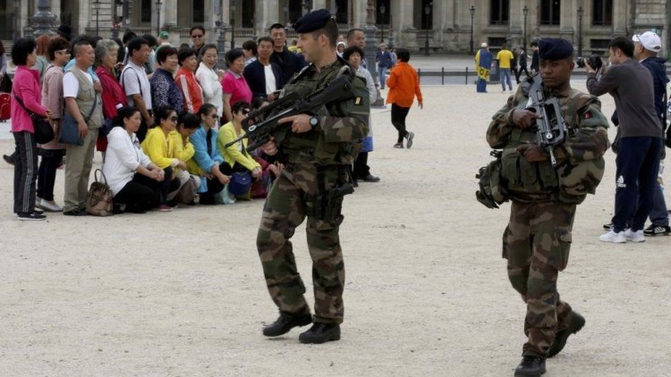 Chinese tourists take group pictures as French army soldiers patrol near the Louvre Museum Pyramid's main entrance in Paris (19 August 2016)