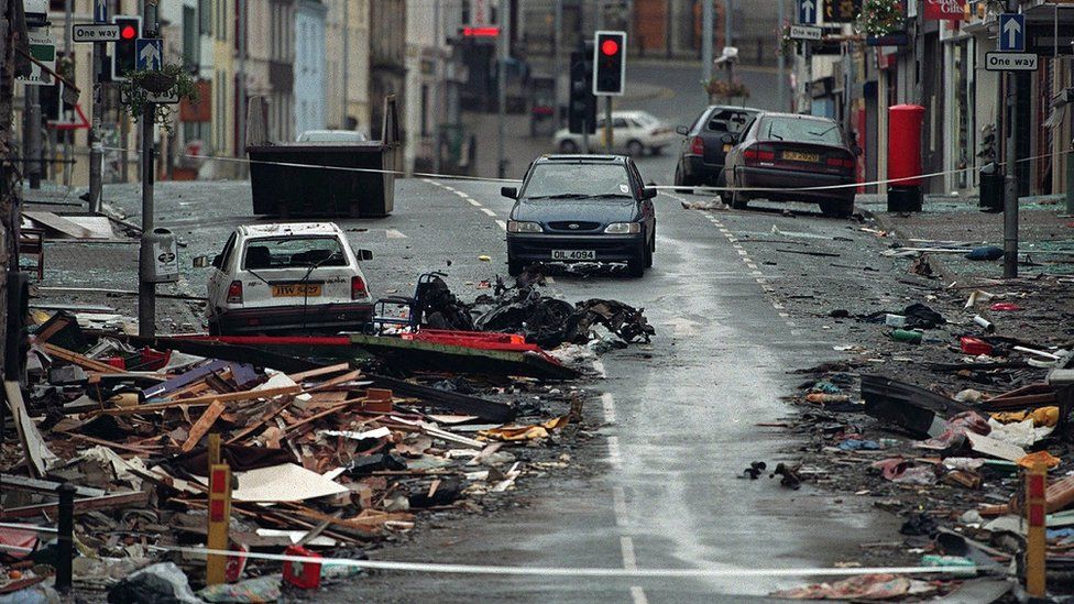 The aftermath of Omagh bombing in 1998. Debris is strewn across the road around a white and a dark blue car