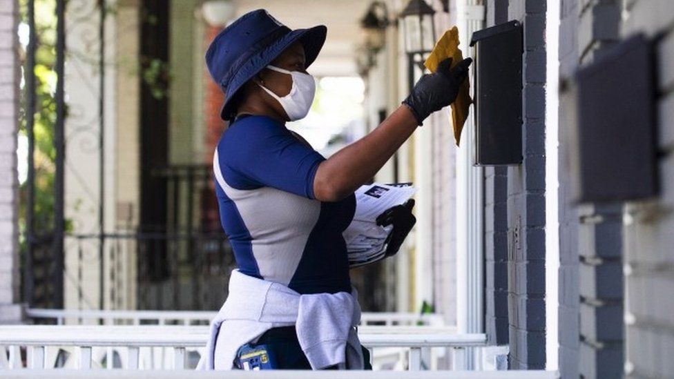 A US Postal Service worker puts mail in a letter box