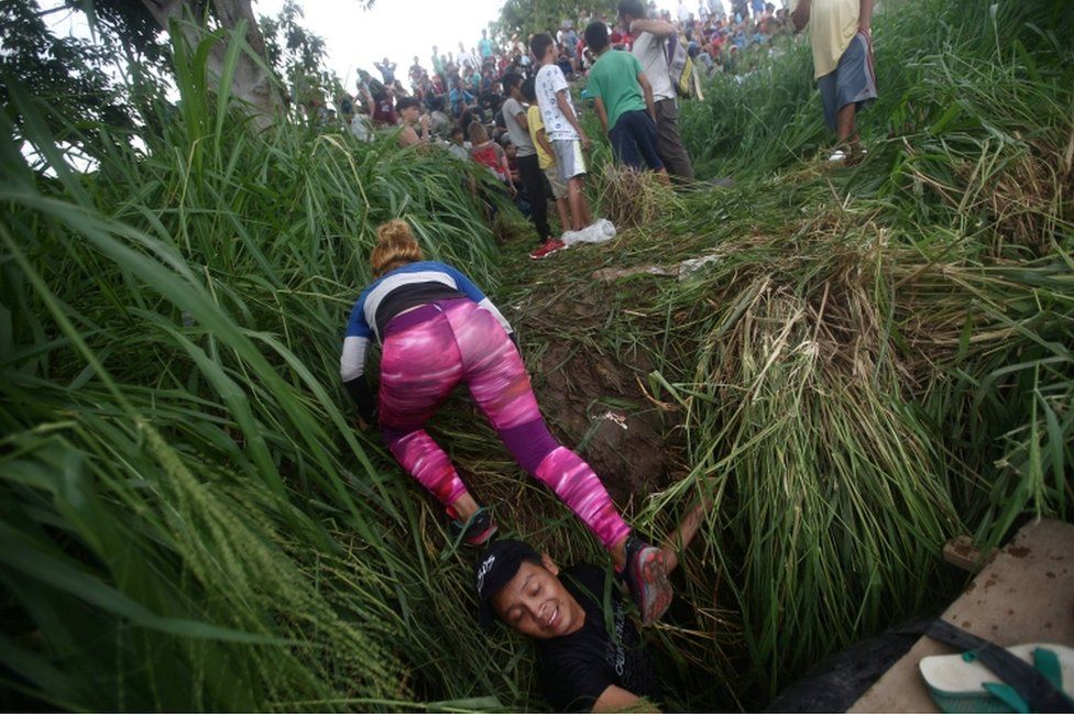 A woman crawls onto the riverbank after crossing the Suchiate River with the help of fellow migrants