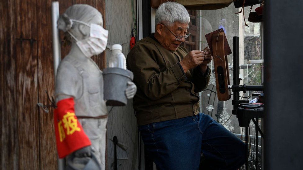An elderly man sews a handmade wallet at an alley in Beijing on October 6, 2022.