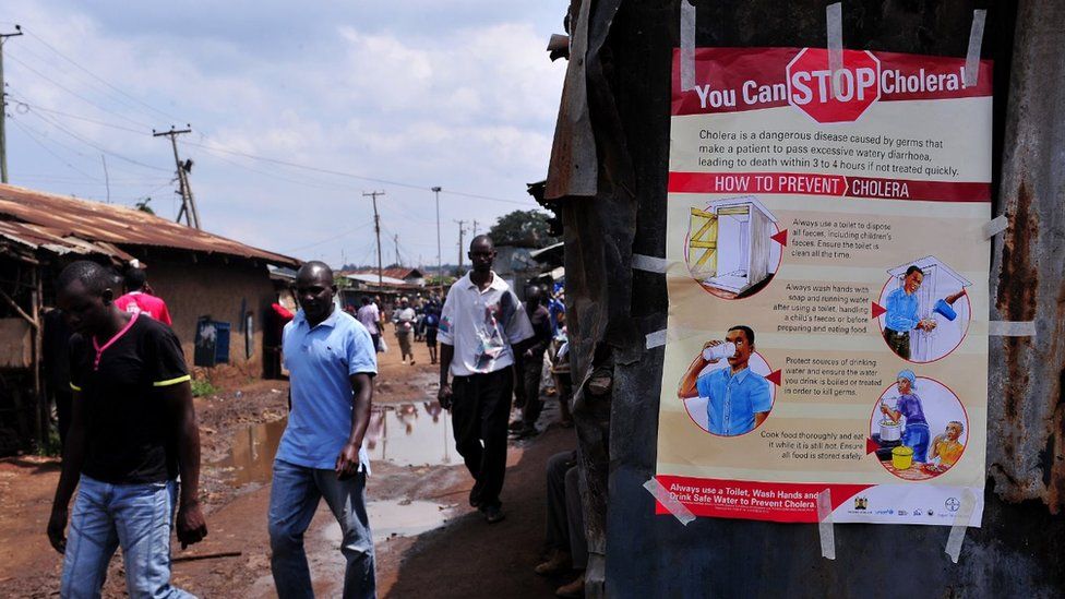 People walk past a kiosk where a poster giving information on how to prevent Cholera is displayed in the Kibera area of Nairobi on May 20, 2015