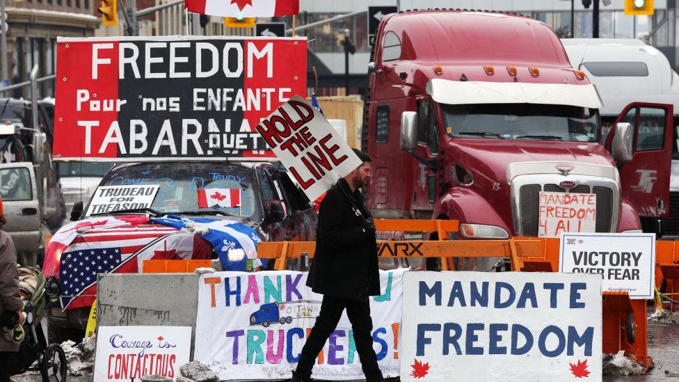 Протестующий идет перед припаркованными грузовиками, поскольку демонстранты продолжают протестовать против мандатов на вакцинацию, введенных премьер-министром Джастином Трюдо 8 февраля 2022 года в Оттаве