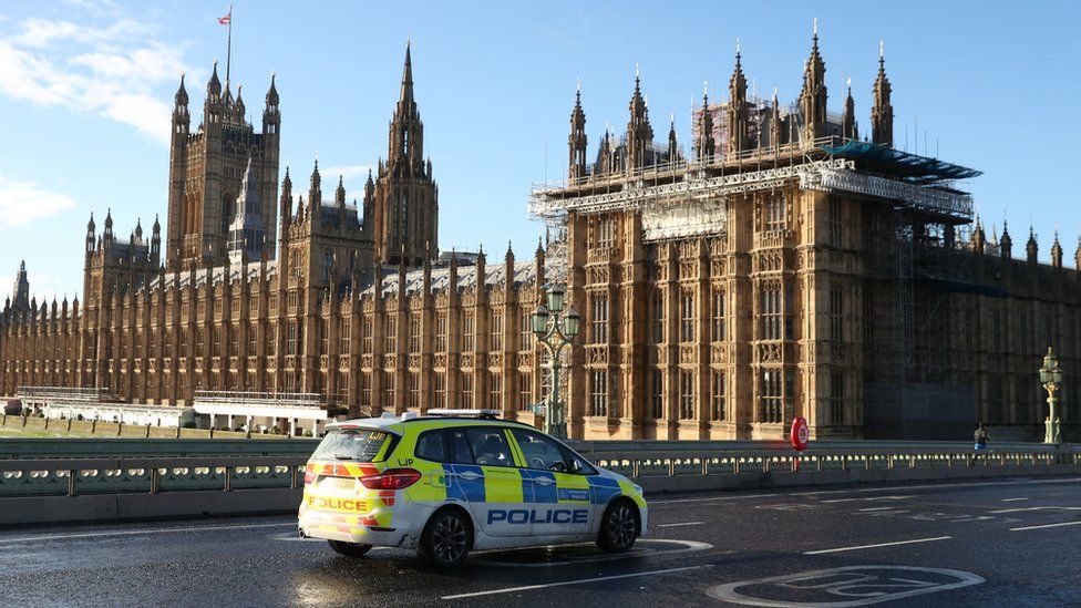 A police car travels over Westminster Bridge near the Houses of Parliament