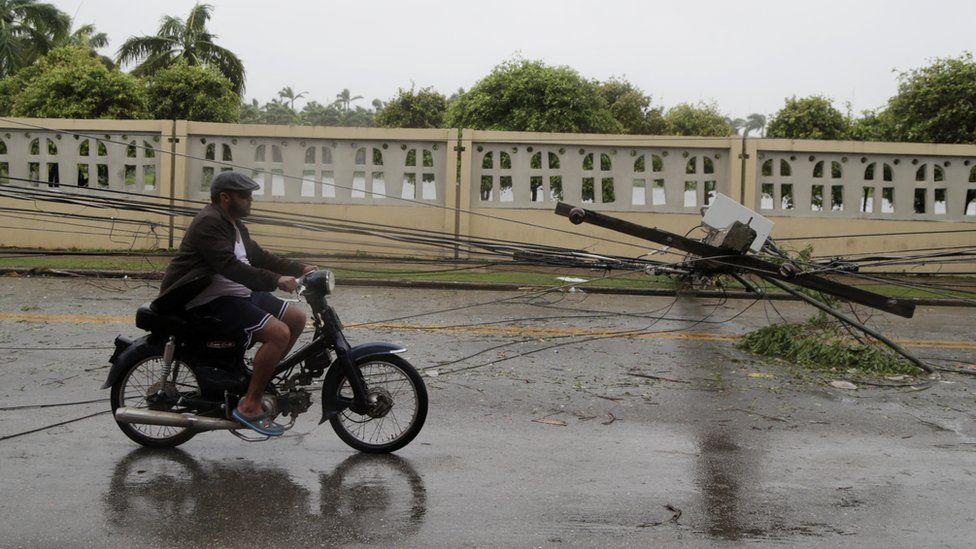 A man rides on a motorcycle past fallen power lines in the Dominican Republic