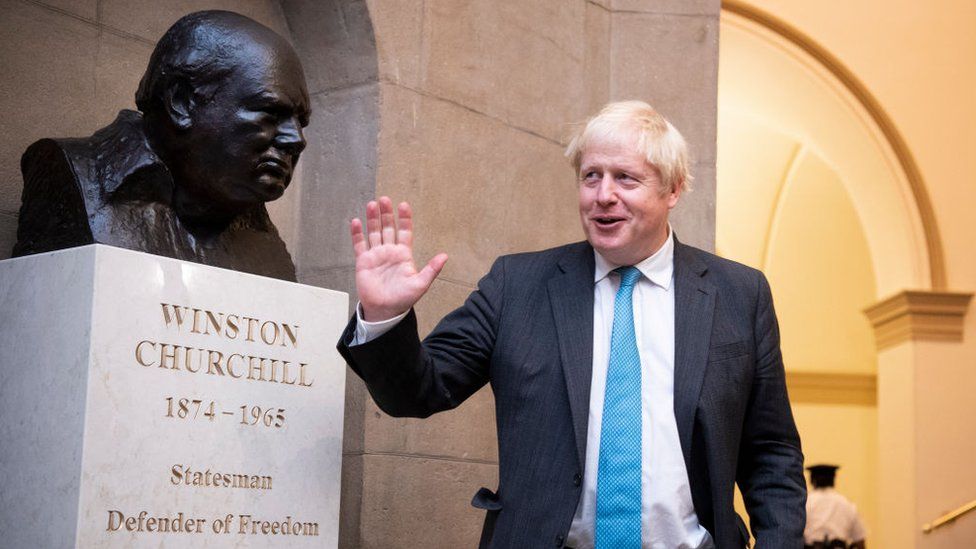 Boris Johnson stood next to a bust of Winston Churchill
