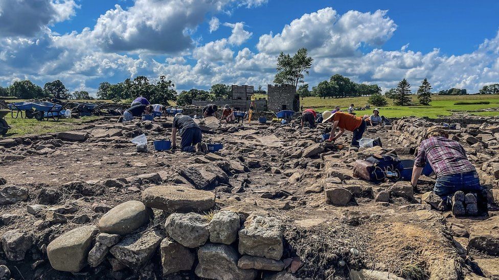 A group of people on their knees digging between rocks and stones at the Roman settlement