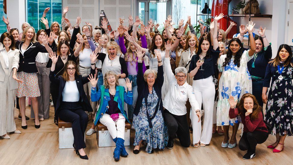 A large group of women waving and smiling at the camera