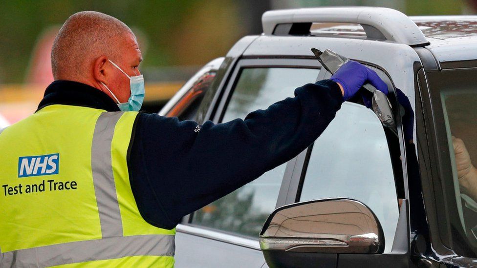 NHS employee hands test kit to person in car