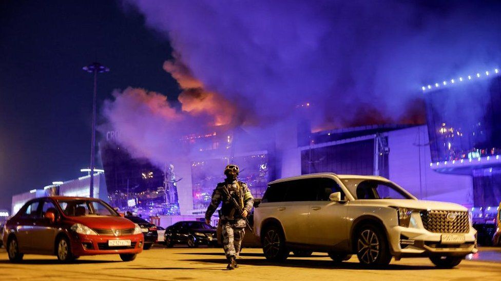A Russian law enforcement officer walks at a parking area near the burning Crocus City Hall