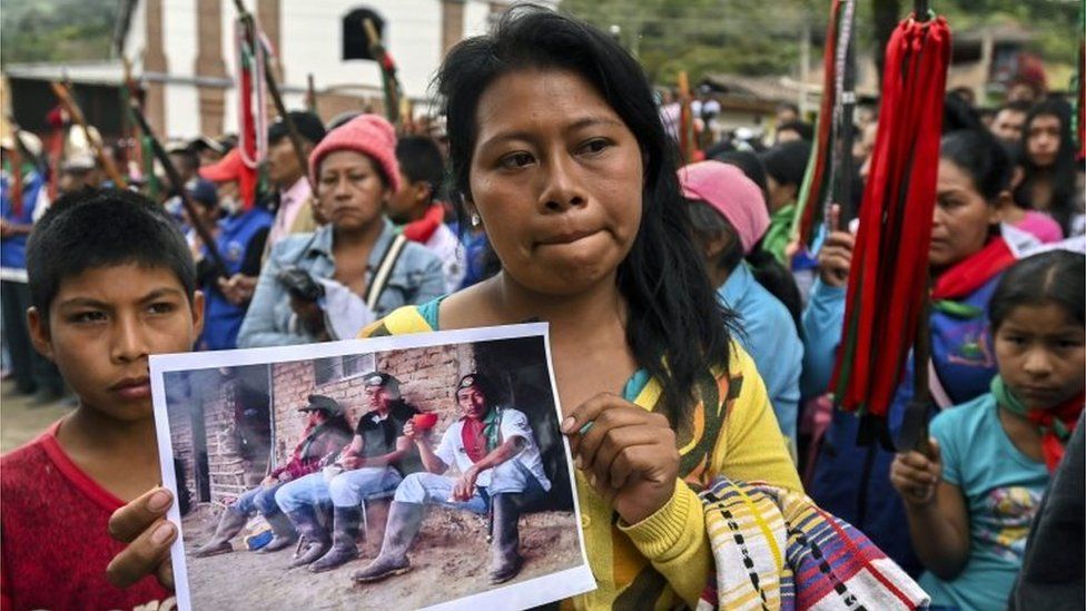 A woman holds up a photo of Kevin Mestizo (centre) and Eugenio Tenorio, who were killed during an attack in Toribio