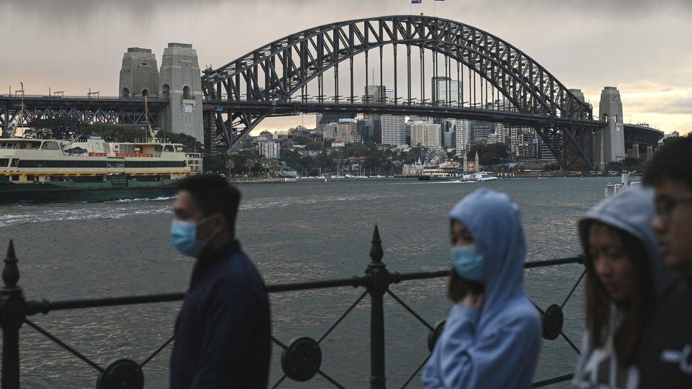 Masked people walk in front of the Sydney Harbour Bridge