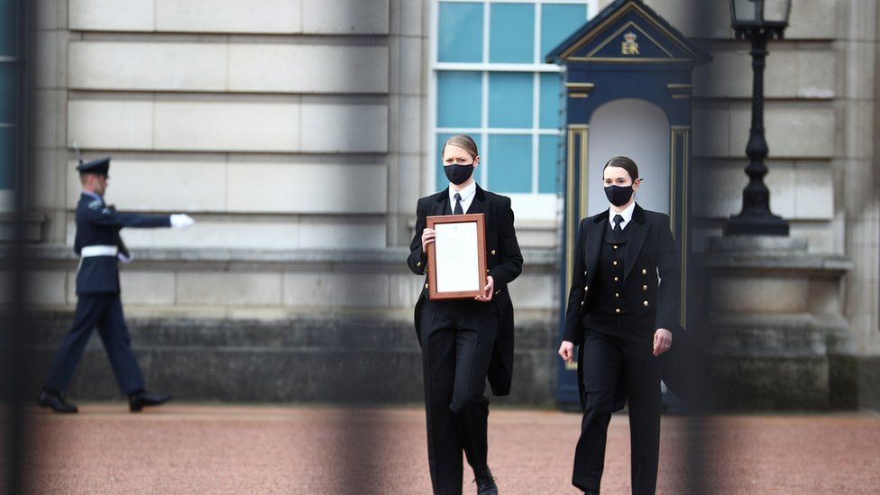 Staff members bring a notice to the fence of Buckingham Palace after it was announced Prince Philip had died