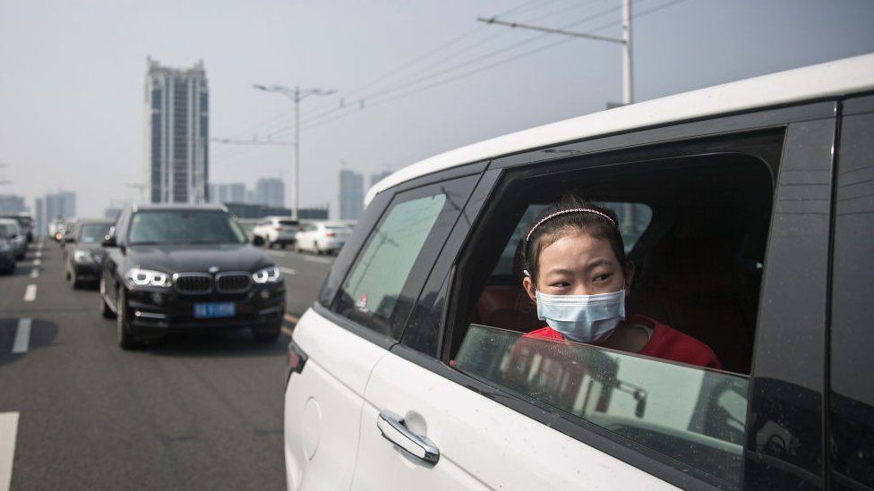A girl sits in car while traffic stops during a silent tribute to those who died of coronavirus in Wuhan.
