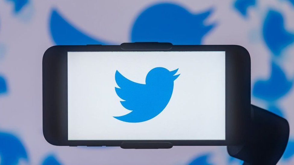 Twitter logo displayed on a smartphone in front of a Twitter logo background