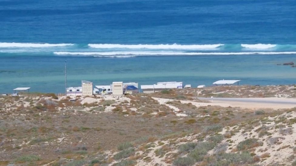 Police cars and trailers near the beach shacks of the campsite