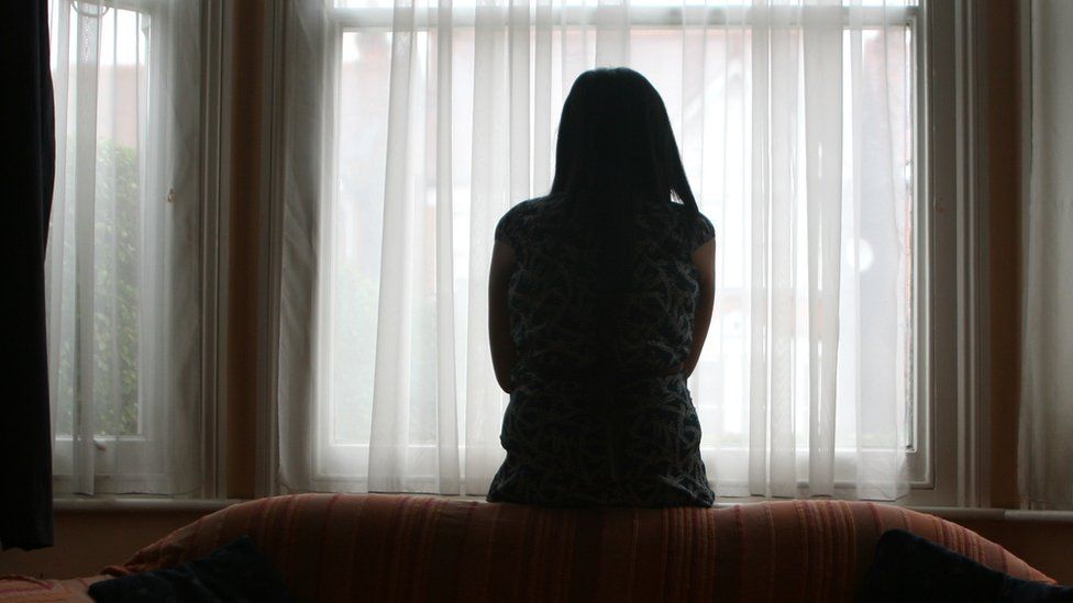 A file photo of a silhouetted woman standing alone in the bay window of a house