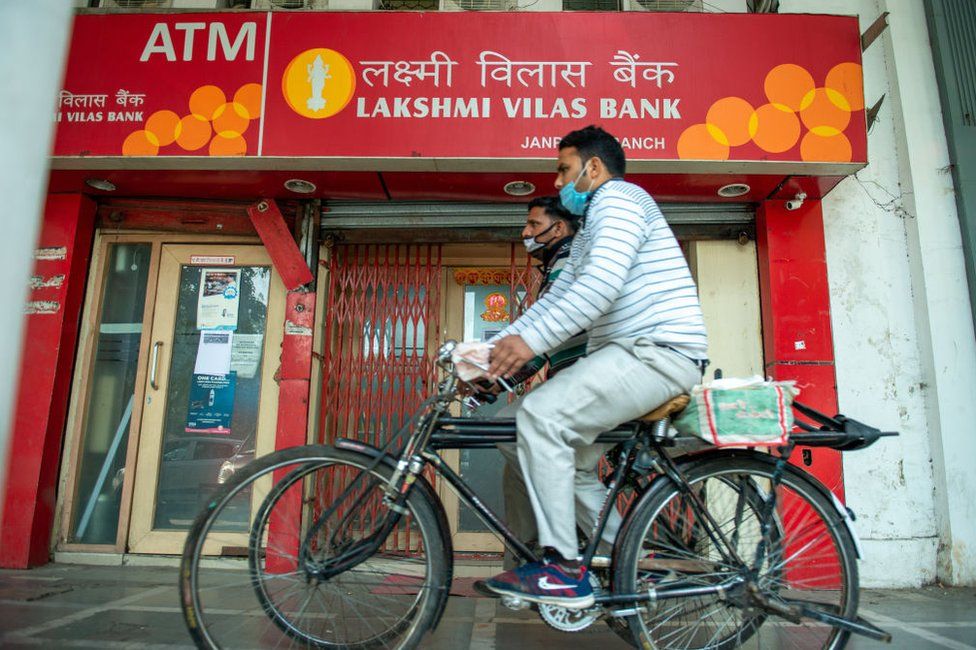 Men on bicycles wearing face masks ride past Connaught place branch of Lakshmi Vilas bank.