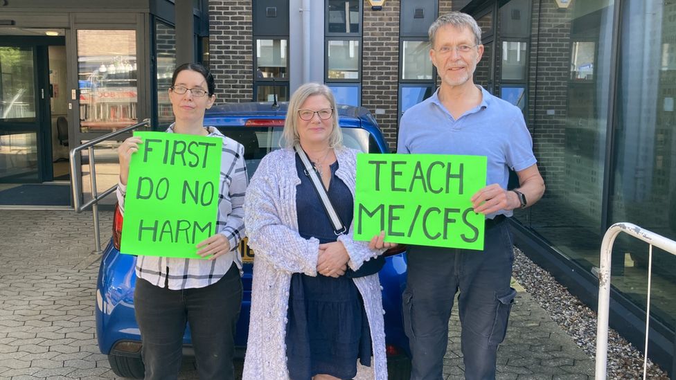 Three protesters holding green neon signs saying First Do No Harm and Teach ME/CFS