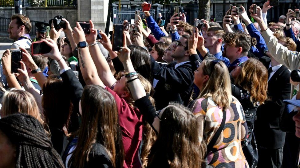 Dozens of people hold their phones as they try to take a photo or video of King Charles and Camilla as they arrive at St Anne's Cathedral