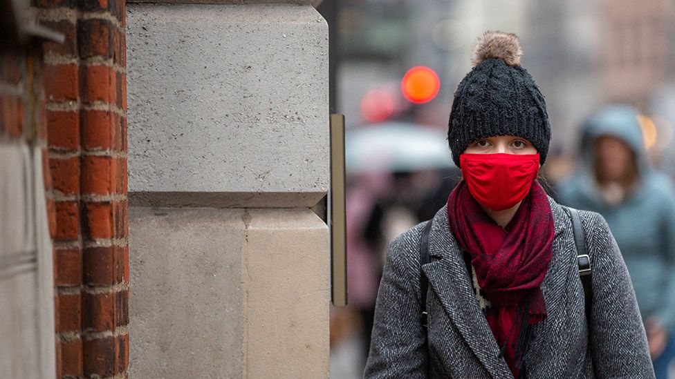 Woman walking down Piccadilly wearing a red mask, 5 December