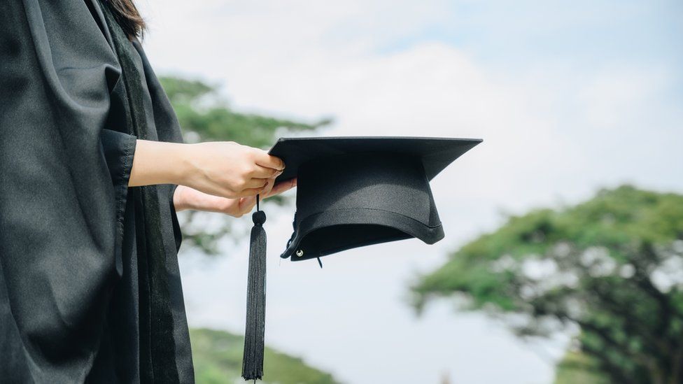 a person in a black graduation gown holding a cap