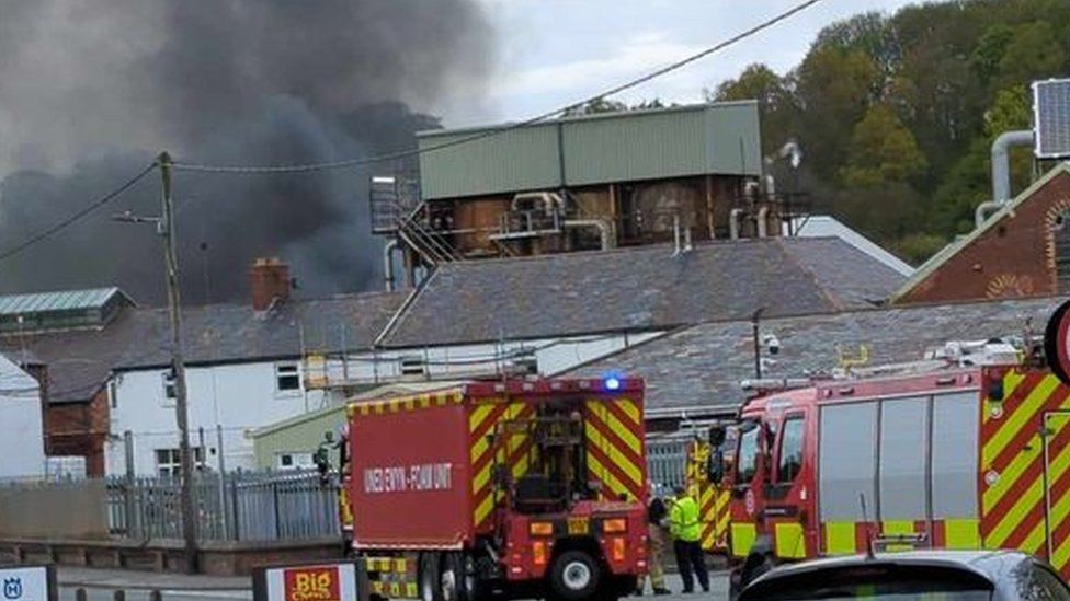 Dark black smoke and fire crews in front of some buildings