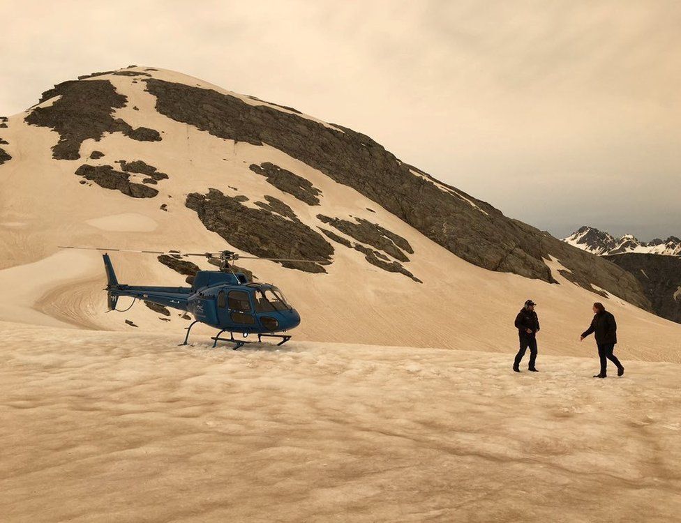 A helicopter and two people are seen on snow