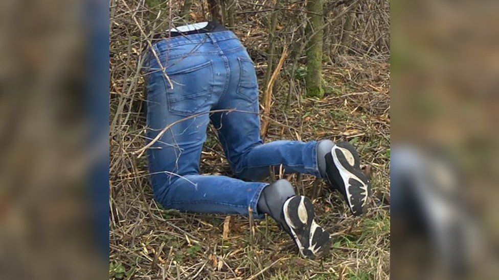 A pair of mannequin legs kneeling in a hedge