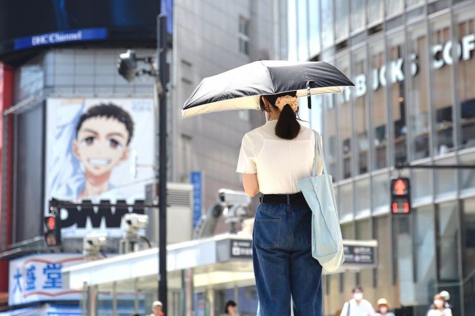A young woman is seen on the street using an umbrella to protect herself from the midday sun on June 27, 2022, in Tokyo's popular Shibuya district in Tokyo, Japan.