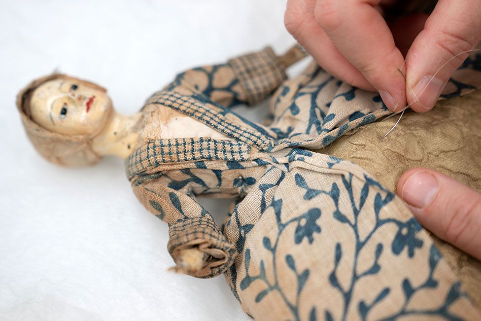 A textile conservator stitches the clothing of a doll from the Uppark dolls' house at the National Trust Textile Conservation Studio in Norwich, UK