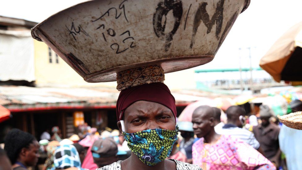A woman wearing a face mask and carrying a dish on her head in Lagos, Nigeria - May 2020