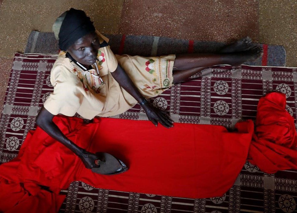 Woman sitting on the floor ironing a red fabric.