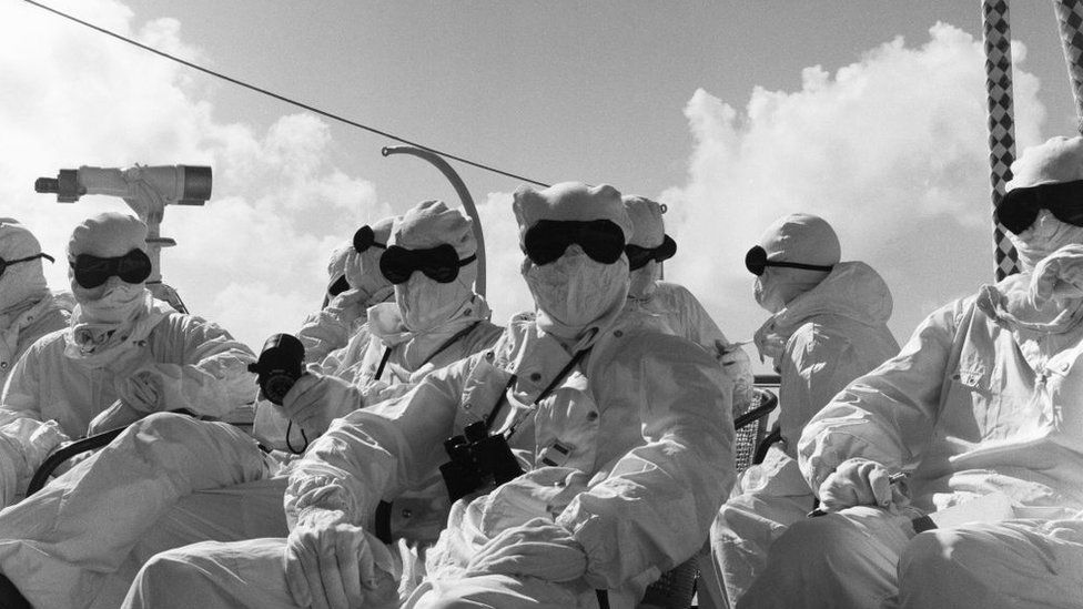 Members of the press and naval ratings aboard HMS Alert 35 miles offshore of Malden Island, Kiribati dressed in protective suits. The ships crew and passengers where there to witness the second test of Britain's Hydrogen bomb. 31st May 1957