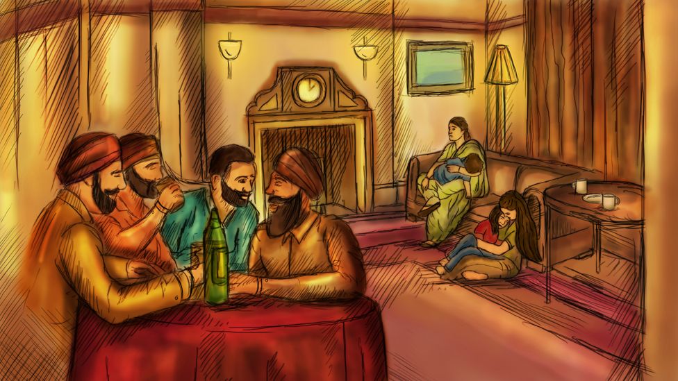 A group of men drink spirits at a table while women look after tired children in the background