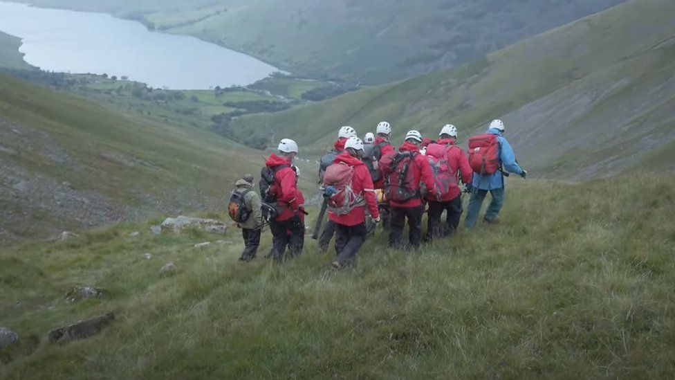 Six rescuers carry stretcher with Daisy on it overlooking lake