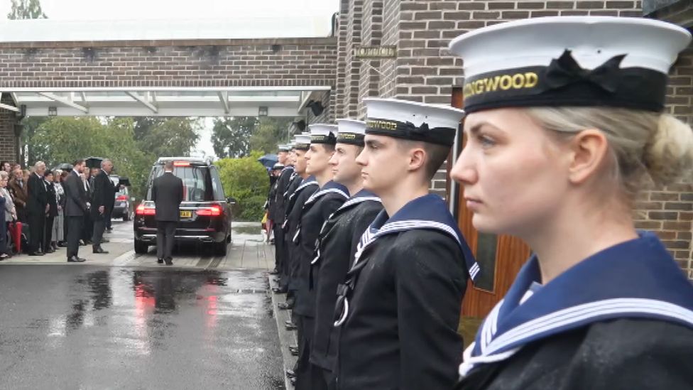 Armed Forces staff standing in line as coffin is walked past