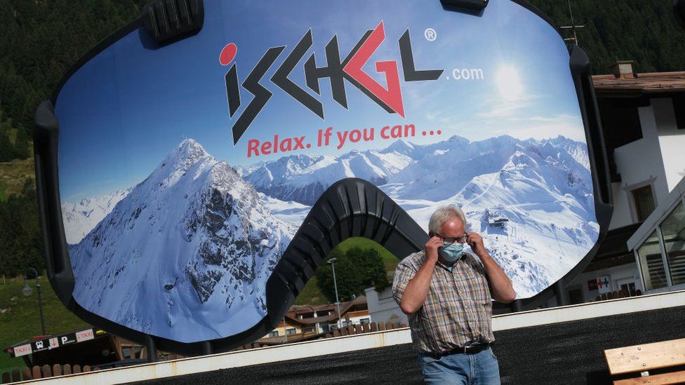 A man removes a protective face mask after photographing himself in front of an advertisement in the shape of ski goggles for the Ischgl ski resort