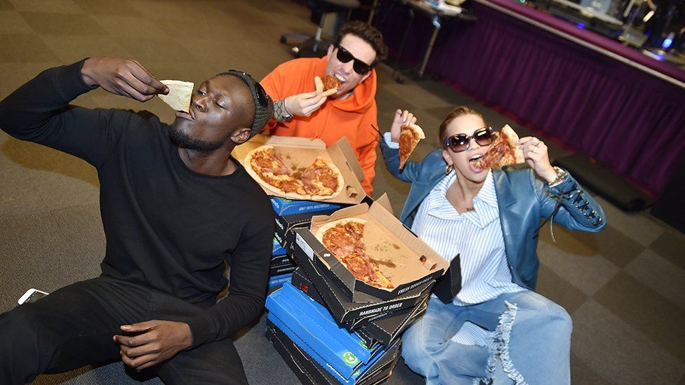 Nick Grimshaw, Rita Ora and Stormzy eating pizza on the floor