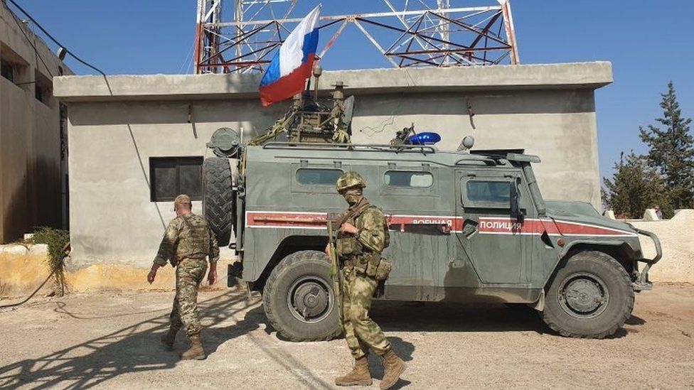 Russian soldiers walk past a Russian military police armoured vehicle at a position in the north-eastern Syrian city Kobane on 23 October 2019