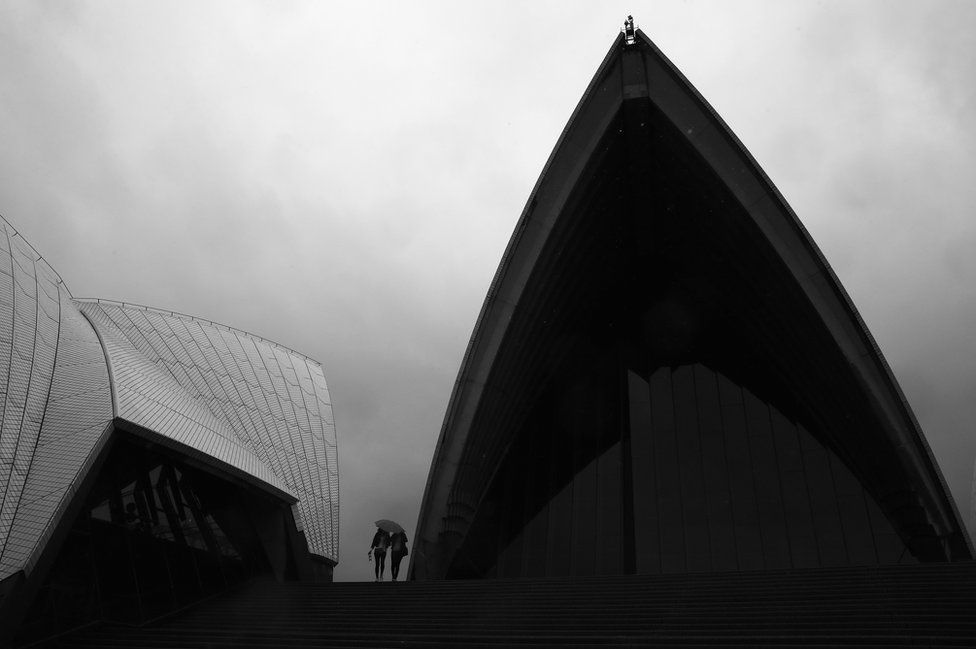 Two people share an umbrella to shelter outside the Sydney Opera House