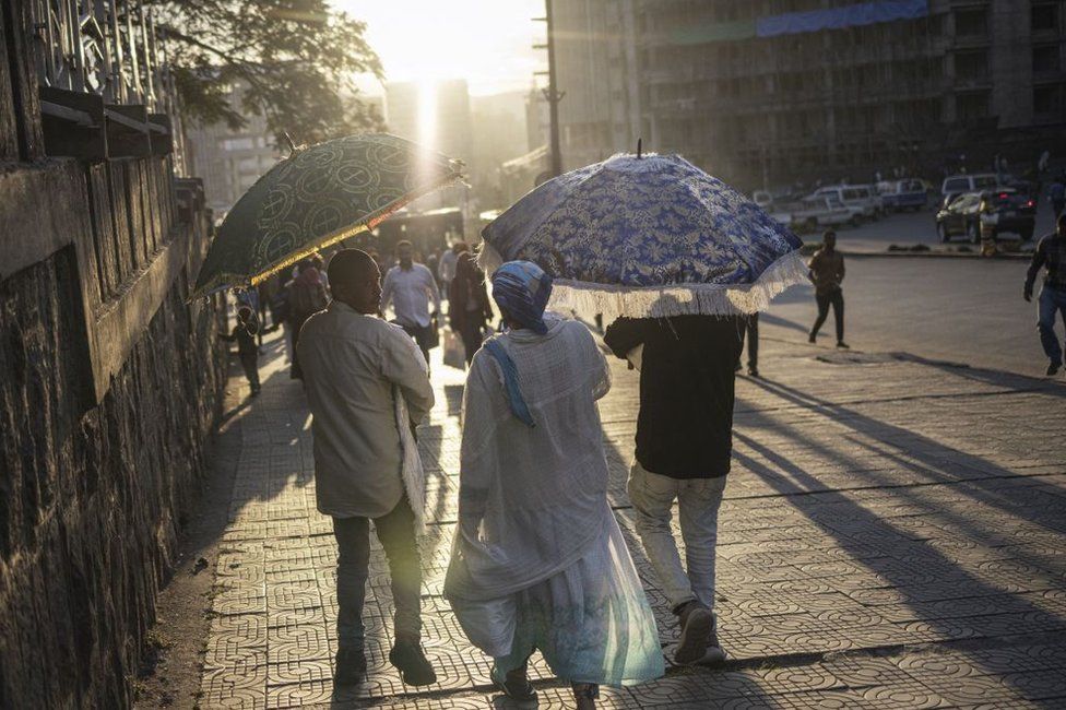 Ethiopian Orthodox Christians walk down the street, wearing white clothes and carrying embroidered umbrellas.