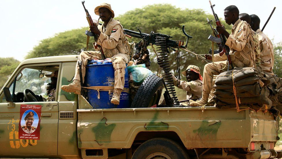 Rapid Support Forces holding guns while driving in the back of a pick-up truck