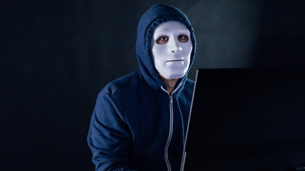 A man in a mask behind a laptop