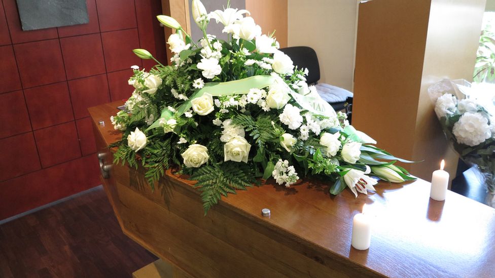 Flowers and candles sit on top of a coffin
