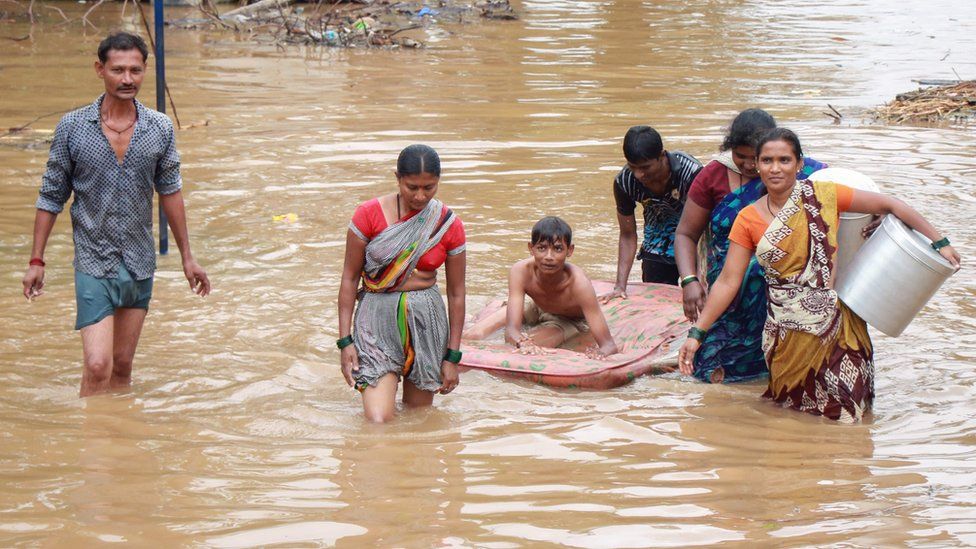 People wade through floodwaters to reach higher ground following heavy rains in Karnataka state on 8 August