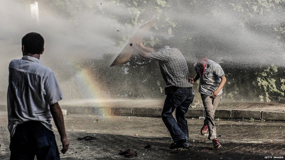 Left-wing militants take cover from a water cannon during clashes with Turkish police officers on 25 July