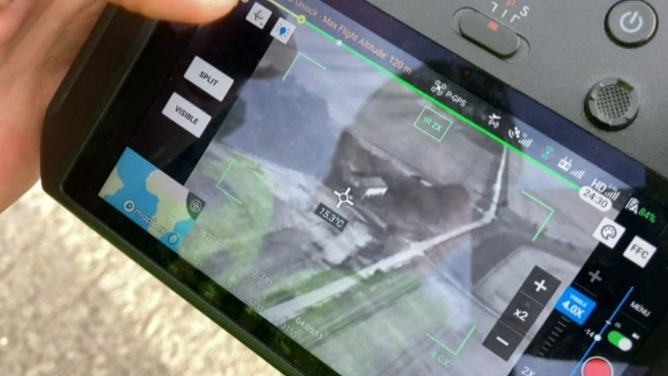 A police drone control console displays thermal images of farm buildings