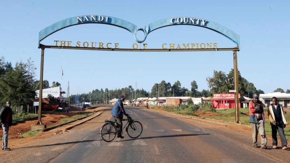 A cyclist runs under a "The Source of Champions" sign near the home of cross-country skier Agnes Tirop before her funeral in the village of Kapnyamisa, Nandi County